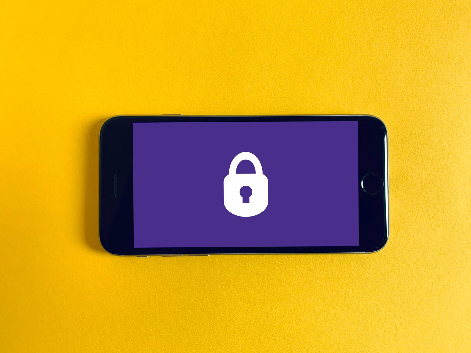 Smartphone showing a white padlock icon on a purple screen, lying on a yellow background